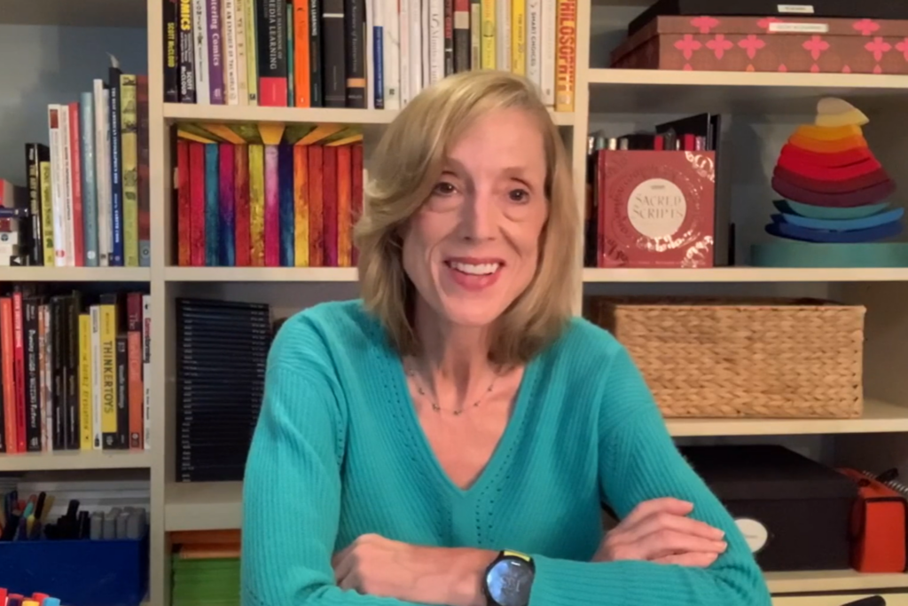 Sue J. Goldie sitting at desk with arms folded, smiling at camera