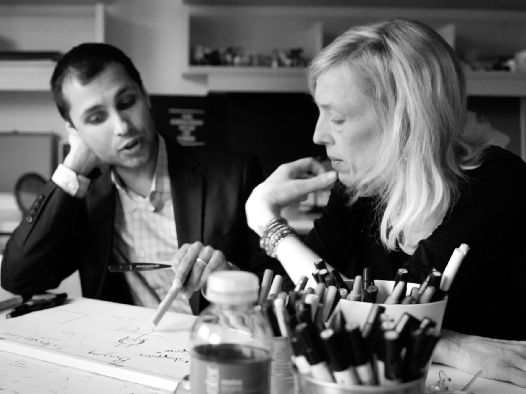 Ankur Pandya (left) and Sue J. Goldie (right) in conversation while seated at desk with Goldie writing on paper 