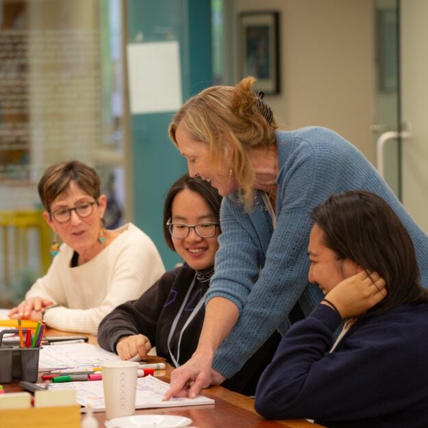 Sue Goldie leans over table and points at paper between seated attendees (You Wu and Ryenchindorj Erkhembayar)