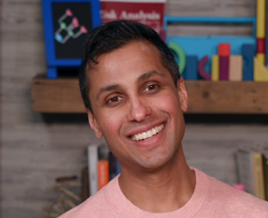 Headshot of Ankur Pandya. Background includes colorful objects on wood shelves