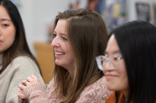 Photo of student seated at conference room table smiling off camera